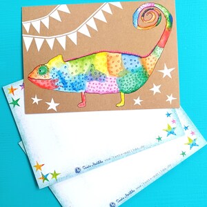 May include: A colorful watercolor illustration of a chameleon on a brown card, with white stars and a banner. Two matching envelopes with star accents are below. The chameleon is painted in rainbow hues.