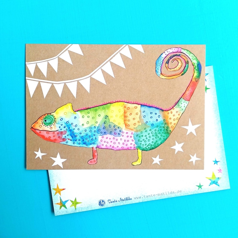 May include: A colorful watercolor illustration of a chameleon on a kraft paper card. The chameleon is depicted in vibrant rainbow hues with a curled tail. White star and banner decorations surround the chameleon. A second card with star accents is visible.