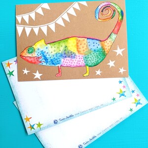 May include: A colorful watercolor illustration of a chameleon on a brown card, with a rainbow of colors. White stars and a banner decorate the card. Two white envelopes with star accents are in the foreground.