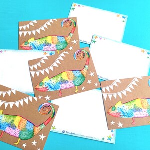 May include: A collection of stationery cards featuring a colorful chameleon design. The chameleon is depicted in a patchwork style with vibrant rainbow colors. The cards have a kraft paper background with white star and banner accents.