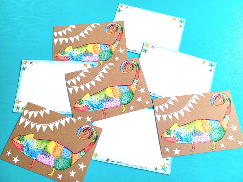 May include: A collection of stationery cards featuring a colorful chameleon design. The chameleon is depicted in a patchwork style with vibrant rainbow colors. The cards have a kraft paper background with white star and banner accents.