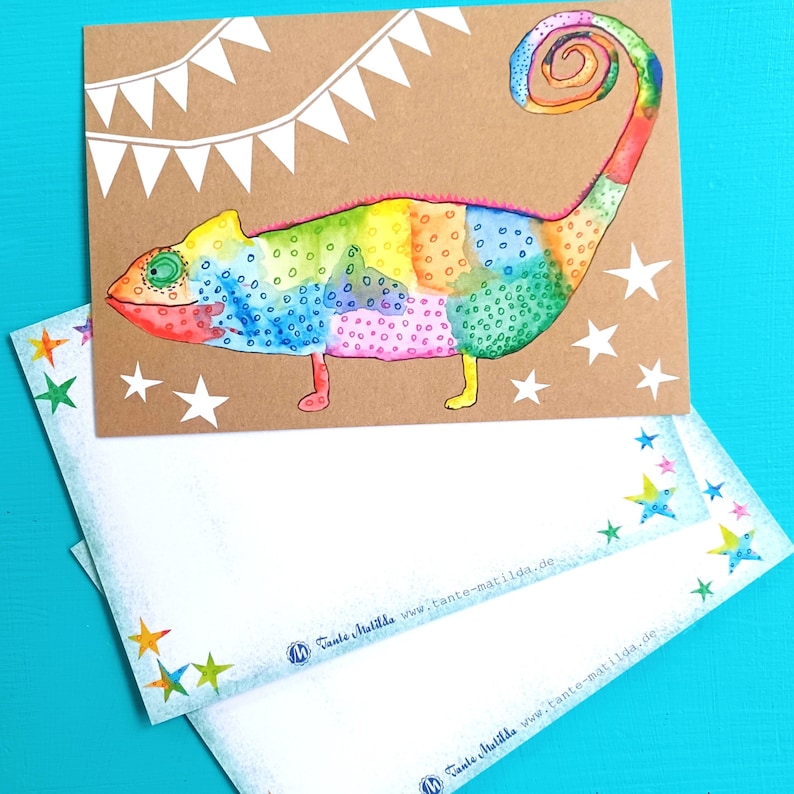 May include: A colorful watercolor illustration of a chameleon on a brown card, with white stars and a banner. Two matching envelopes with star accents are below. The chameleon is painted in rainbow hues.