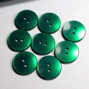 Op de afbeelding: Acht groene plastic knopen met elk twee gaten. De knopen hebben een glanzende, licht iriserende afwerking.