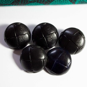 Könnte beinhalten: Fünf schwarze Knöpfe mit gewebter Textur. Die Knöpfe sind rund und haben ein leicht erhabenes Design.