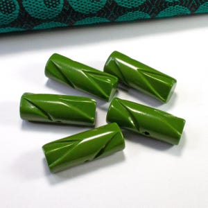 Op de afbeelding: Vijf groene plastic knopen met een gedraaid ontwerp. De knopen zijn ongeveer 2,5 cm lang en hebben een gat in het midden.