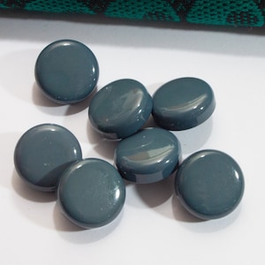 Könnte beinhalten: Eine Gruppe von sieben runden, dunkelgrauen Knöpfen. Die Knöpfe sind glatt und glänzend.