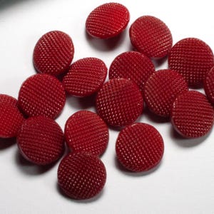 Könnte beinhalten: Eine Sammlung von 15 roten Knöpfen mit einer strukturierten Oberfläche. Die Knöpfe sind rund und haben eine glänzende Oberfläche.