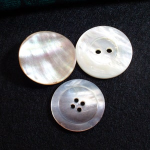 May include: Three white mother-of-pearl buttons. One button has two holes, and the other two buttons have four holes.