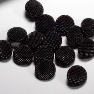 Könnte beinhalten: Eine Sammlung schwarzer Knöpfe mit einer strukturierten Oberfläche. Die Knöpfe sind rund und haben eine glänzende Oberfläche.