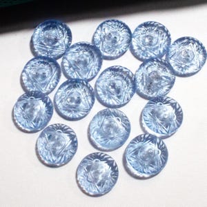 Könnte beinhalten: Eine Sammlung von 15 hellblauen Glasknöpfen mit einem Sternendesign. Die Knöpfe sind rund und haben eine erhabene Mitte.