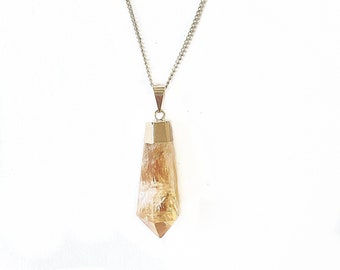 May include: A gold chain necklace with a light brown crystal point pendant.
