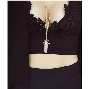 Puede incluir: Un top negro de encaje con un collar de cadena dorada con un colgante de cristal transparente.