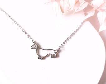 Puede incluir: Un collar de plata con un colgante en forma de silueta de dachshund.