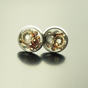Könnte beinhalten: Ein Paar silberne Ohrstecker mit einem runden, klaren Glasdesign, das ein braunes und weißes steampunk-inspiriertes Muster aus Zahnrädern und Uhrwerk zeigt.