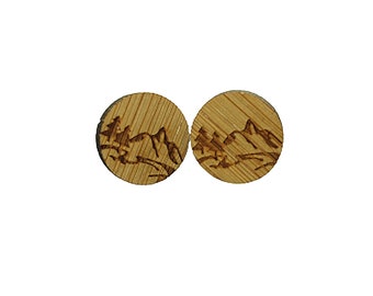 May include: A pair of wooden earrings with a laser-etched design of mountains and trees. The earrings are round and have a natural wood finish.