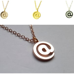 Könnte beinhalten: Eine Halskette aus Gold, Silber und Roségold mit einem Anhänger in Form eines @-Zeichens.