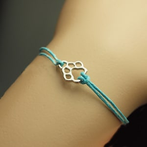 Könnte beinhalten: Ein türkisfarbenes Armband aus Schnur mit einem silbernen Pfotenabdruck-Anhänger.