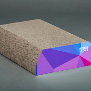 May include: A brown cardboard cat scratching post with a curved top. The top is covered in a colorful geometric pattern with purple, blue, and pink accents. The text "HOUSE OF CATS" is printed in white on the side.