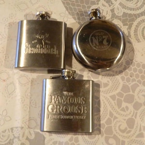 Peut inclure: Trois flasques à alcool en acier inoxydable. L'une est rectangulaire avec le logo Glenfiddich, l'une est circulaire avec le logo Old No. 7 Brand, et l'une est rectangulaire avec le texte The Famous Grouse Finest Scotch Whisky gravé.