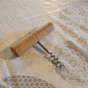 Pode incluir: Um saca-rolhas em forma de T com um cabo cilíndrico de madeira castanho-claro e uma espiral metálica. O cabo apresenta uma inscrição estampada claramente visível que diz "MADE IN ITALY" ao longo da sua lateral.