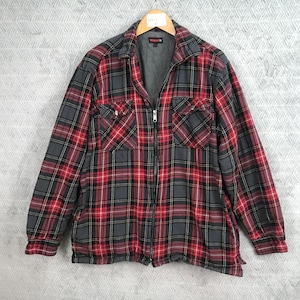 Könnte beinhalten: Eine rot-schwarz-graue Flanelljacke mit Karomuster und durchgehendem Reißverschluss. Die Jacke hat zwei Brusttaschen mit Knopfverschluss und ein graues Fleecefutter. Die Jacke hängt an einem Holzbügel.