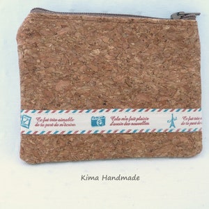 May include: A cork fabric zippered pouch with a white and blue striped ribbon with French text and images of a camera and the Eiffel Tower. The text reads "Ce fut très aimable de ta part de m'écrire" and "Cela m'a fait plaisir d'avoir des nouvelles". The pouch is labeled "Kima Handmade".