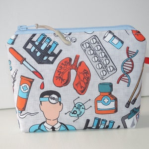 Könnte beinhalten: Eine graue Reißverschlusstasche mit einem hellblauen Reißverschluss und einem roten Zugband. Die Tasche ist mit verschiedenen medizinischen Illustrationen verziert, darunter ein Arzt, Lungen, Pillen, Reagenzgläser und eine DNA-Sequenz.