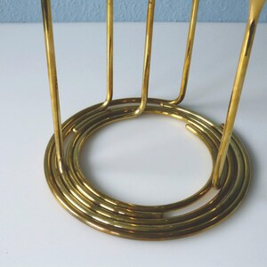 Puede incluir: Un soporte de metal dorado con una base circular y m&uacute;ltiples soportes verticales. El soporte est&aacute; dise&ntilde;ado para sostener varios art&iacute;culos, como vasos o botellas.