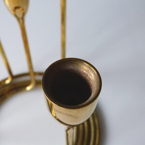 Puede incluir: Un candelero de metal dorado con tres portavelas. El candelero tiene una base circular y un dise&ntilde;o en espiral.