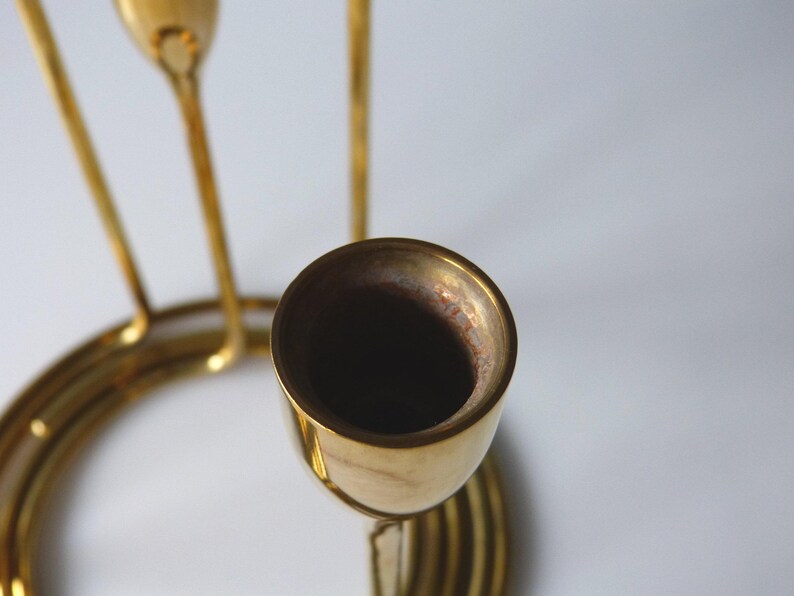 Puede incluir: Un candelero de metal dorado con tres portavelas. El candelero tiene una base circular y un dise&ntilde;o en espiral.