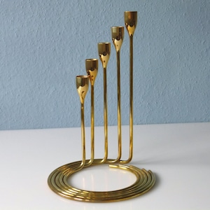 Puede incluir: Un candelero de metal dorado con cinco brazos que se enrollan en una base circular.