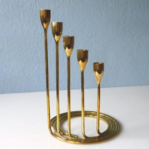 Puede incluir: Un candelero de metal dorado con cinco brazos dispuestos en espiral. El candelero est&aacute; hecho de una sola pieza de metal y tiene un acabado pulido.