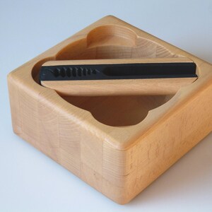 May include: A wooden nutcracker with a black handle and a built-in storage compartment. The nutcracker is made of light wood and has a simple, elegant design.