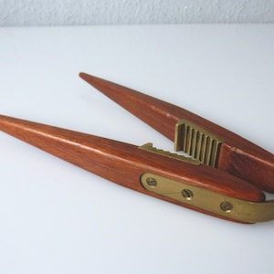 May include: A wooden nutcracker with brass accents. The nutcracker is shaped like two long, pointed pieces of wood that come together to crack nuts.