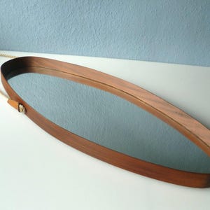 May include: Oval wooden mirror with a rope handle. The mirror has a light wood frame and a clear reflection.