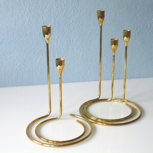 Puede incluir: Un candelero de metal dorado con cinco brazos, cada uno con una parte superior redonda. El candelero est&aacute; dise&ntilde;ado en un estilo moderno con una base curva.