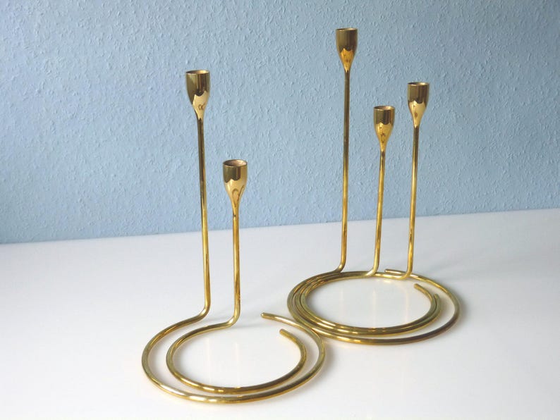 Puede incluir: Un candelero de metal dorado con cinco brazos, cada uno con una parte superior redonda. El candelero est&aacute; dise&ntilde;ado en un estilo moderno con una base curva.