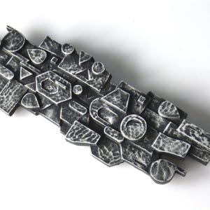 Puede incluir: Una escultura de pared abstracta de metal en blanco y negro. La escultura está compuesta por muchas formas y tamaños diferentes, y tiene una superficie texturizada.