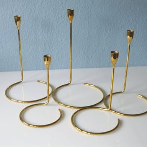 Puede incluir: Un juego de cuatro candelabros de metal dorado con un dise&ntilde;o moderno. Los candelabros est&aacute;n conectados en un patr&oacute;n circular, creando una pieza central &uacute;nica y elegante.