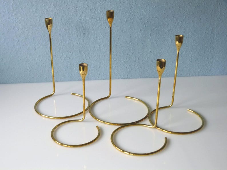 Puede incluir: Un juego de cuatro candelabros de metal dorado con un dise&ntilde;o moderno. Los candelabros est&aacute;n conectados en un patr&oacute;n circular, creando una pieza central &uacute;nica y elegante.