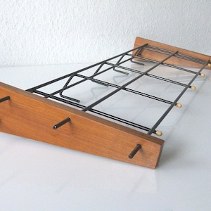 May include: A wall-mounted coat rack with a wooden base and a black metal frame. The rack has multiple hooks for hanging coats, hats, or other items.