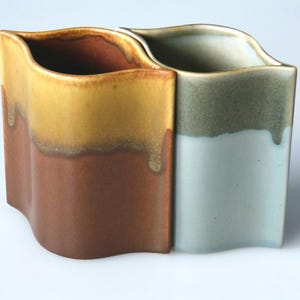 Puede incluir: Dos jarrones de cerámica con un diseño ondulado. El jarrón de la izquierda es marrón, amarillo y naranja. El jarrón de la derecha es azul, verde y blanco.