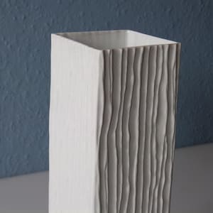 May include: White ceramic vase with a textured, wood-like design. The vase is tall and rectangular.