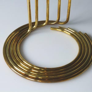 Puede incluir: Un candelero de metal dorado con una base circular y cinco brazos verticales. La base est&aacute; hecha de m&uacute;ltiples anillos conc&eacute;ntricos.