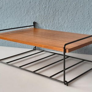 May include: A mid-century modern shelf with a wooden top and a black metal frame. The shelf has a rectangular shape with a lower rack for additional storage. The wooden surface is a warm brown color.