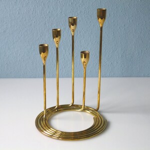 Puede incluir: Un candelero de metal dorado con cinco brazos dispuestos en espiral. El candelero tiene una base circular.