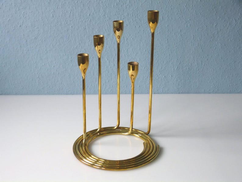 Puede incluir: Un candelero de metal dorado con cinco brazos dispuestos en espiral. El candelero tiene una base circular.