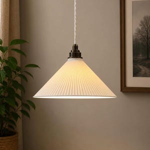 May include: White, cone-shaped pendant light with a ribbed texture. The light fixture hangs from a white cord and has a dark metal fixture at the top. The light is illuminated, casting a warm glow.