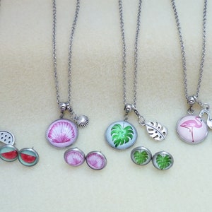 Könnte beinhalten: Fünf silberne Halsketten mit verschiedenen Anhängern, darunter eine Wassermelone, eine Muschel, ein tropisches Blatt, ein Flamingo und ein Paar Ohrringe mit jedem Anhänger.