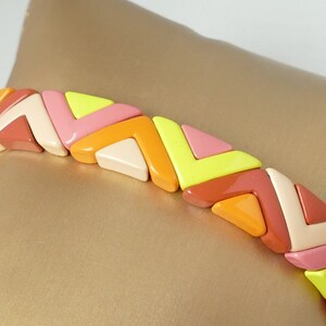 Könnte beinhalten: Ein farbenfrohes geometrisches Armband aus ineinandergreifenden dreieckigen Perlen in den Farben Rosa, Orange, Gelb und Creme.